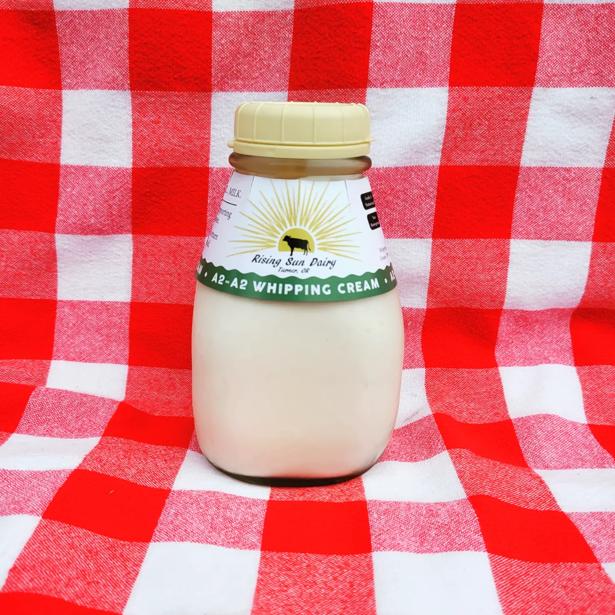 IMG_20221117_123917_048 Bottle of A2-A2 whipping cream from Rising Sun Dairy, set against a red and white checkered background, highlighting its fresh and natural quality.